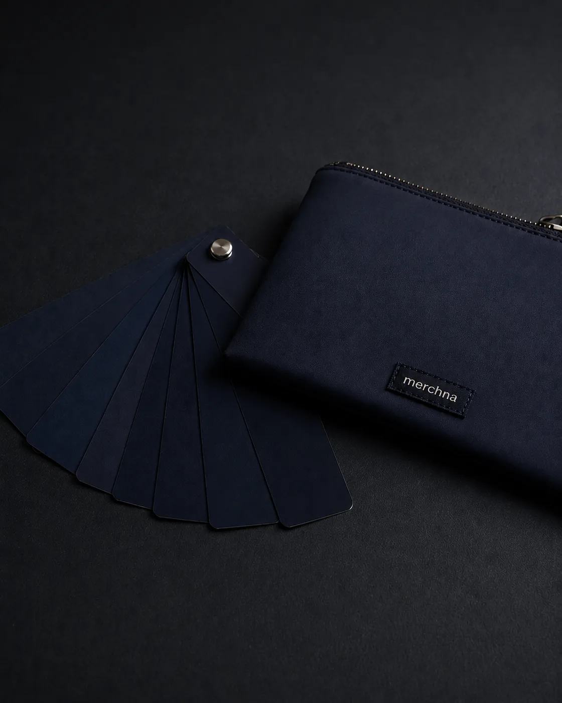 A navy Merchna sample pouch beside a fan of navy fabric swatches for colour matching