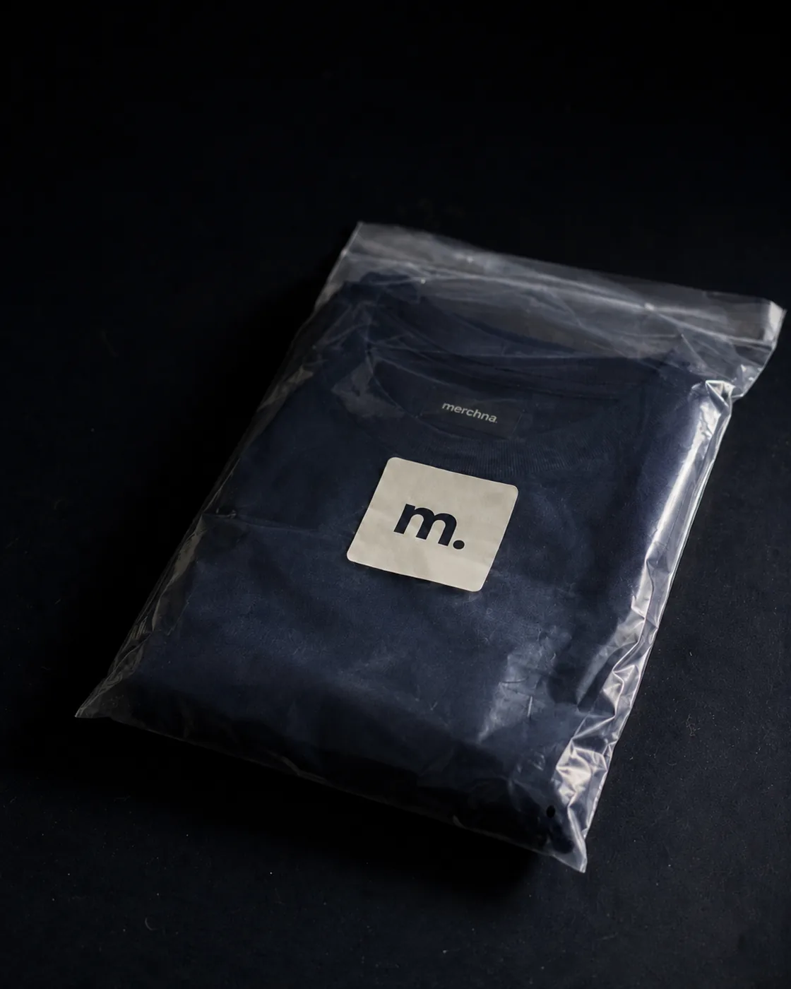 A folded navy Merchna garment packed in a clear polybag with an m. sticker
